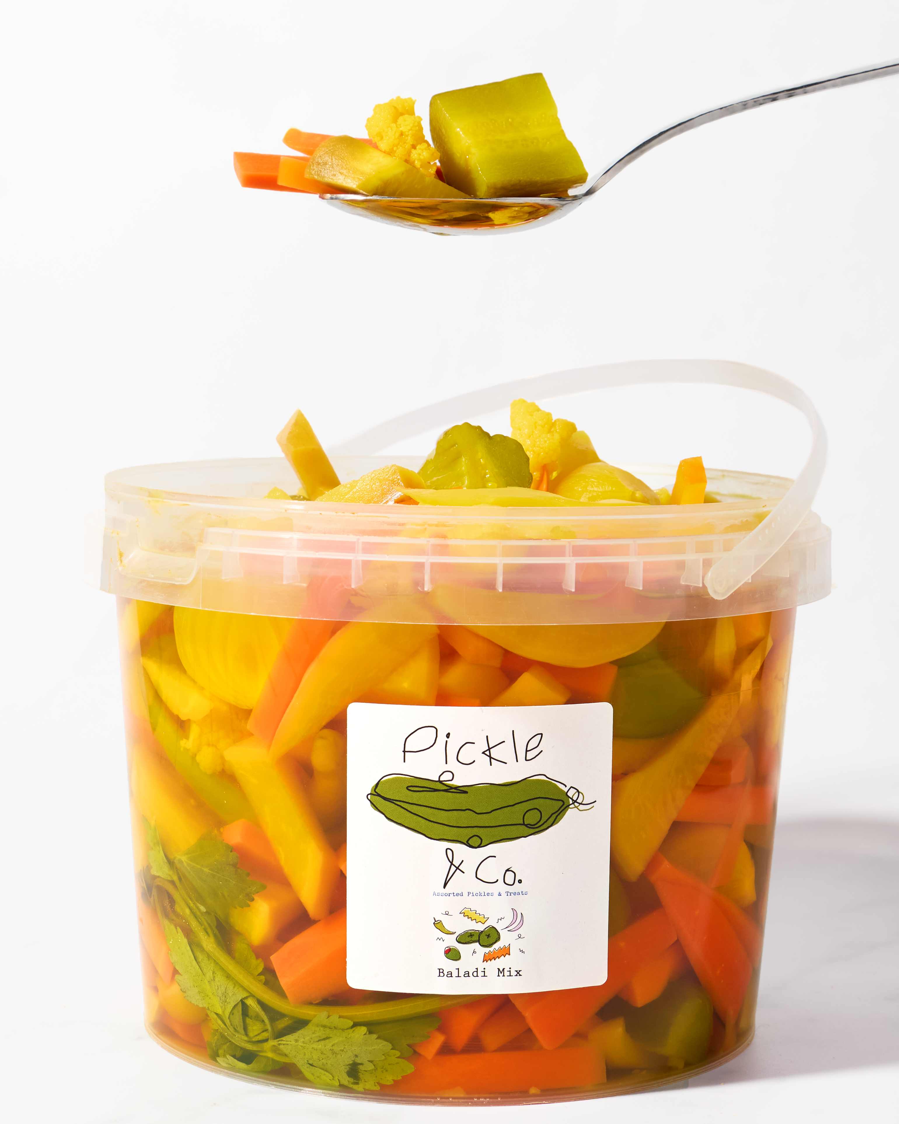 A tub of Pickle & Co. Baladi Mix packed with carrots, turnips and cauliflower, with a spoonful lifted above