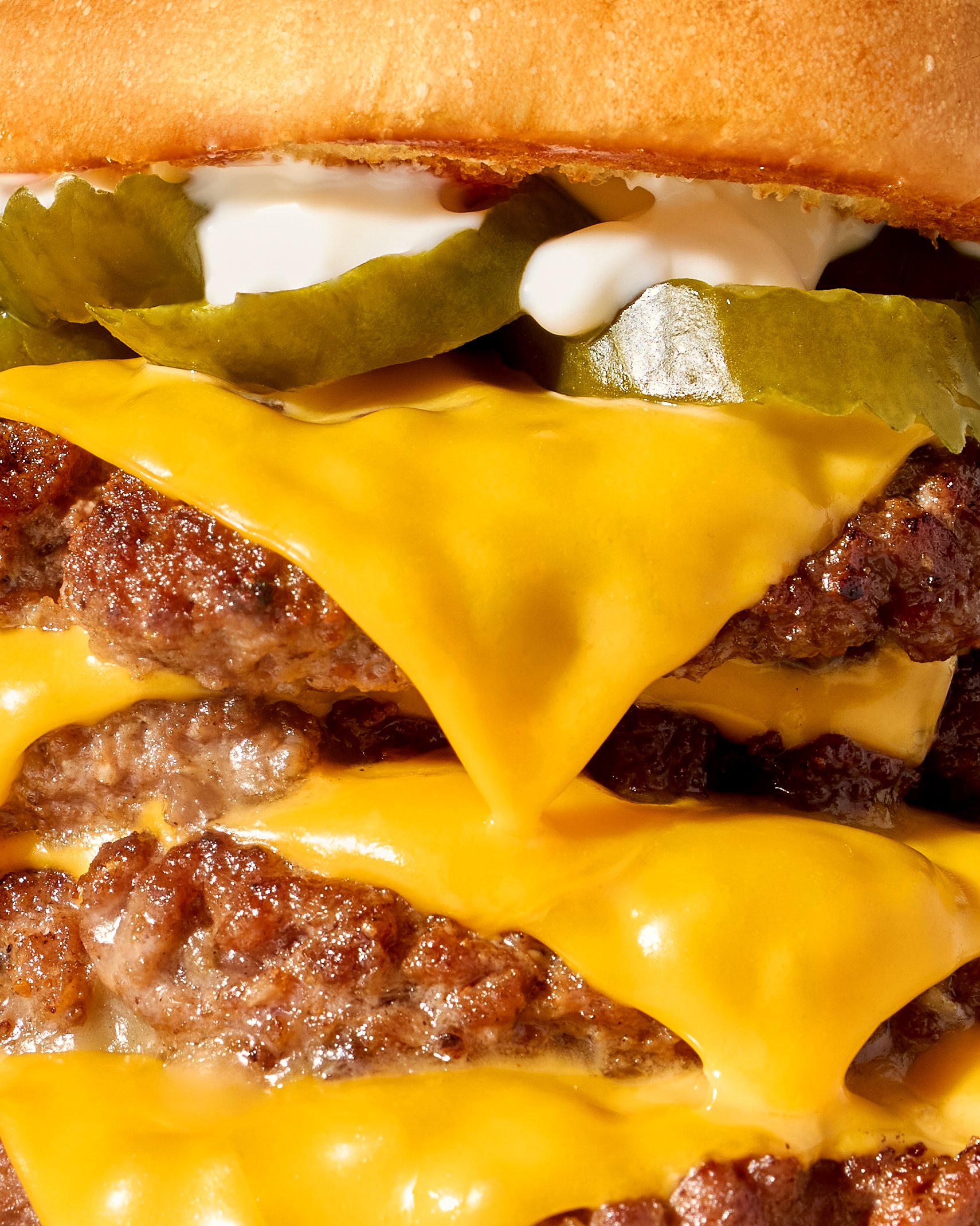 A close-up of a double cheeseburger stacked with pickles, melted cheese and seared beef patties