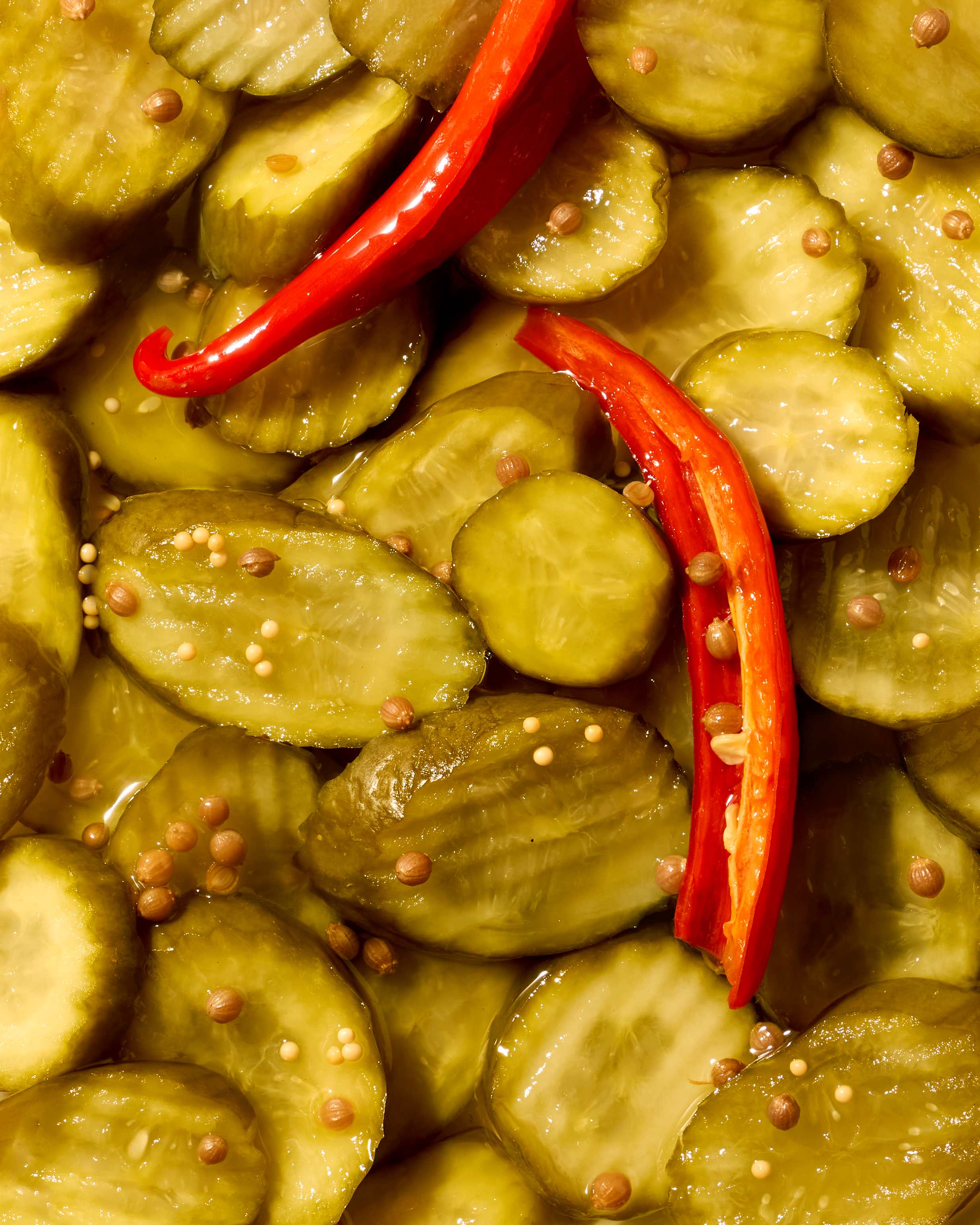 Crinkle-cut pickle slices glistening in brine with split red chilies, coriander and mustard seeds